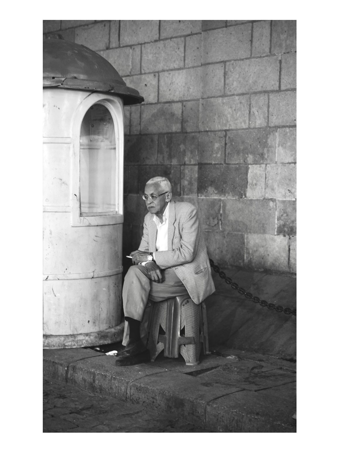 Older man seated beside a stone column