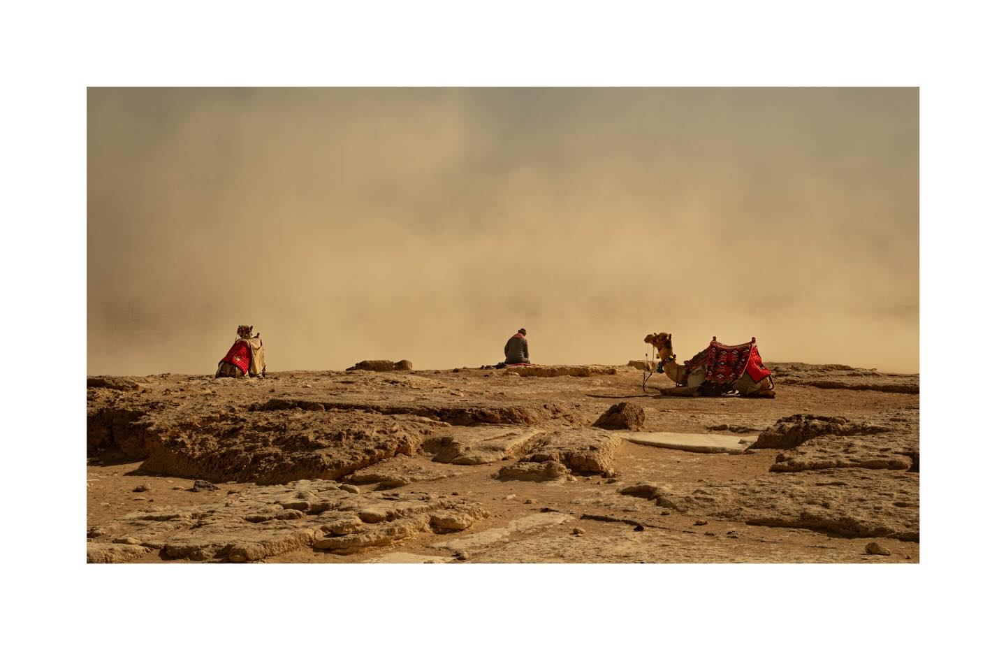 People and camels crossing a desert ridge