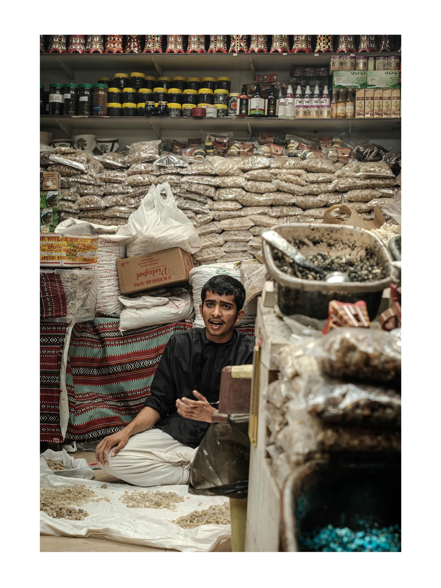 Young shopkeeper seated among sacks and spices