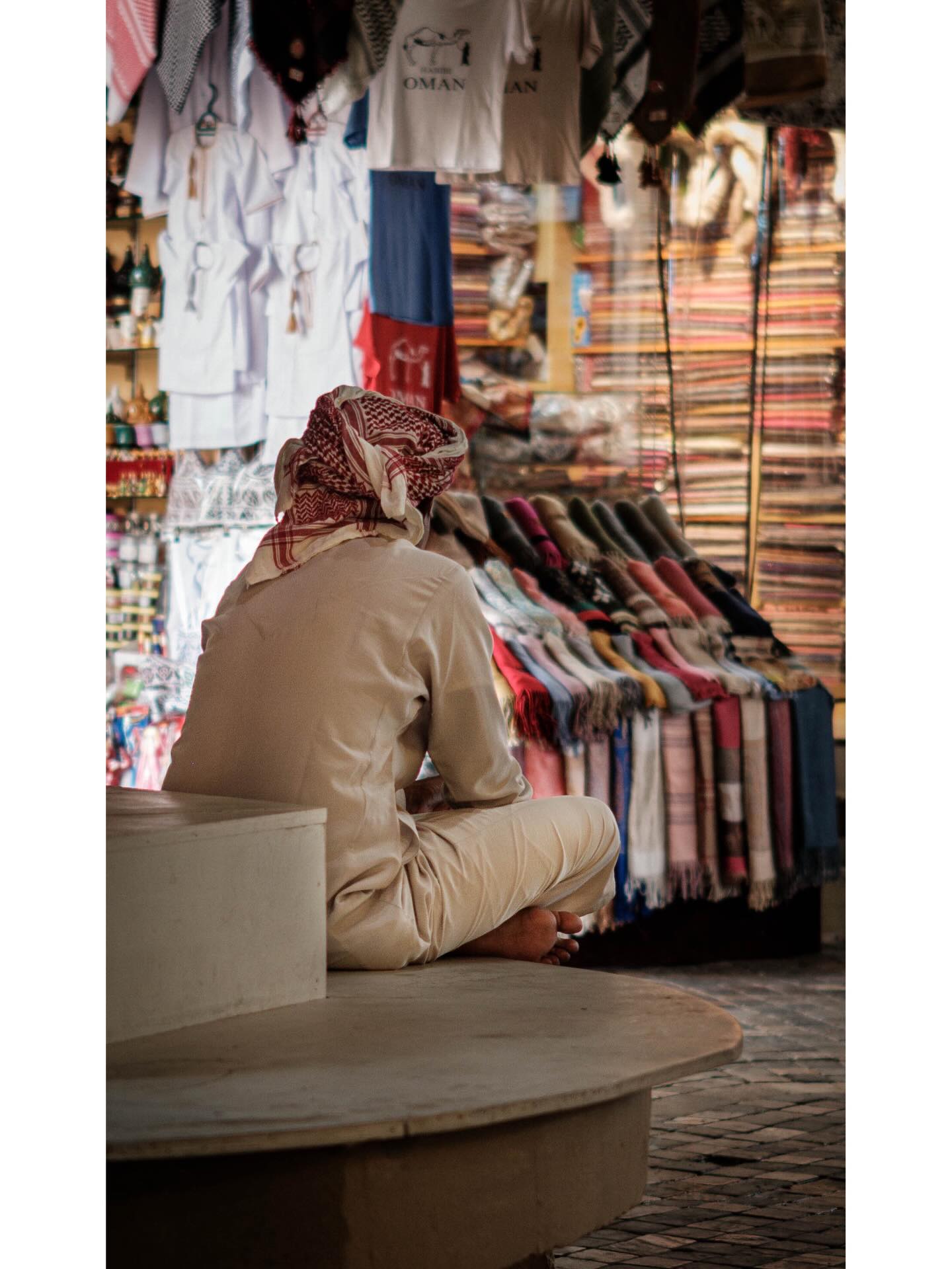 Seated shopkeeper facing hanging textiles