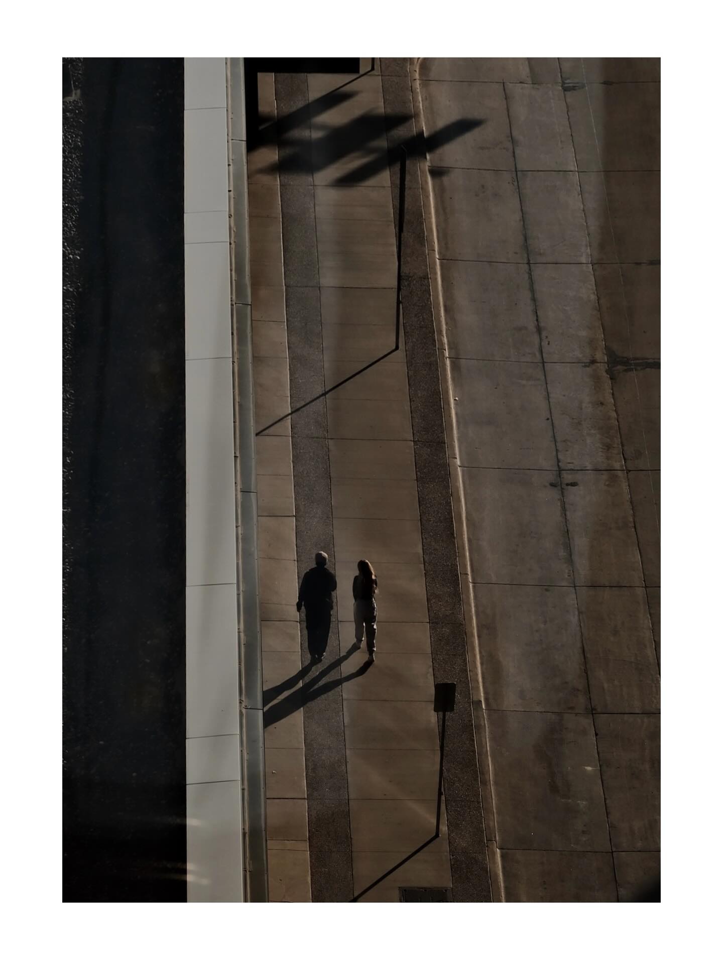 Two people casting long shadows on a sidewalk